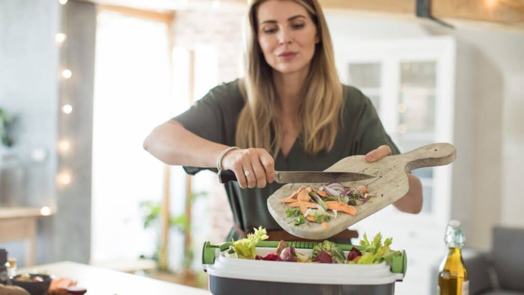 A woman puts vegetable scraps into a compost bin.