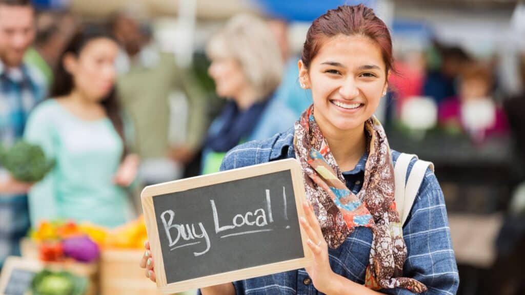 A young woman holds a chalkboard that reads "Buy Local!"